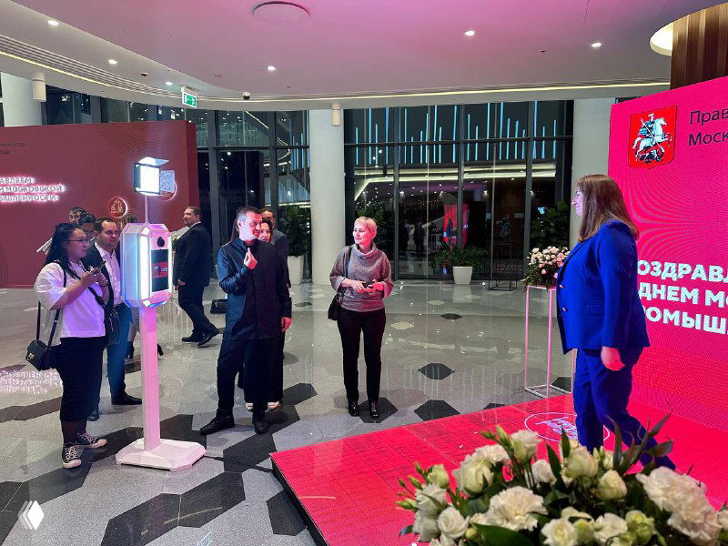 Гости позируют у большой LED‑зоны и фотостойки: яркий красный экран с графикой, фотопринтер и GIF‑стойка на мероприятии.