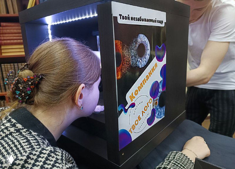 Портативная фотобудка МосФотобудка: человек наклоняется к аппарату для съёмки радужки глаза на мероприятии, видна подсветка и экран.