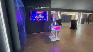 Фотостойка с нейросетью на мероприятии: белая стойка с экраном и розово‑фиолетовой подсветкой в холле, готовая обрабатывать и печатать снимки.