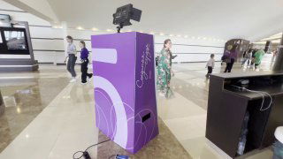 Фиолетовая стойка «селфи-зеркало» в холле мероприятия: корпус с подсветкой и креплением для камеры, гости делают снимки на фоне интерьера и реквизита.