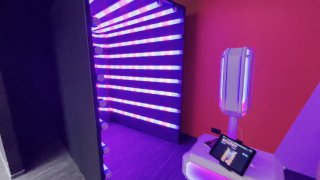 Фотостойка рядом с неоновым туннелем: сенсорный экран и устройство печати на стойке, фиолетово-синие световые полосы в студийном коридоре.