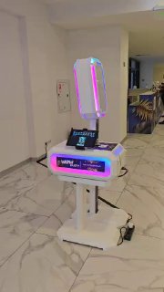 Белая мобильная фотостойка с ИИ в холле: корпус на стойке с RGB‑неоновой подсветкой, сенсорным экраном, цифровой панелью и видимым кабелем питания, демонстрация оборудования для мероприятий.