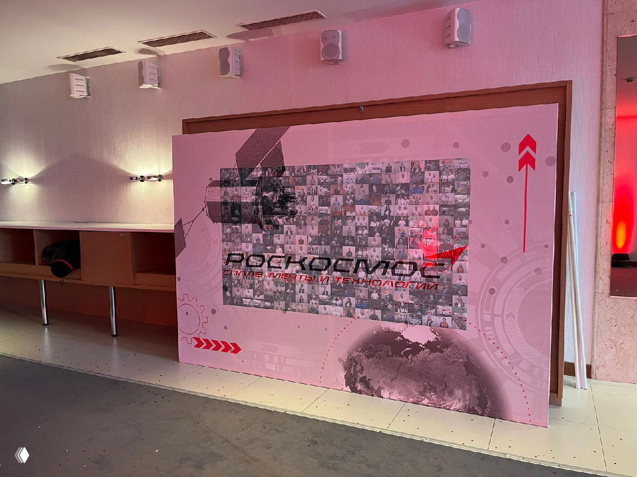 Фотография крупной фотостенки‑мозаики: панно из сотен мини‑фотографий, формирующих фирменный логотип на корпоративном мероприятии.