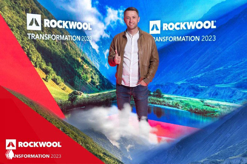 Человек позирует перед яркой LED‑фотозоной с брендированным фоном Rockwool; пример выездной фотозоны и печати на мероприятии