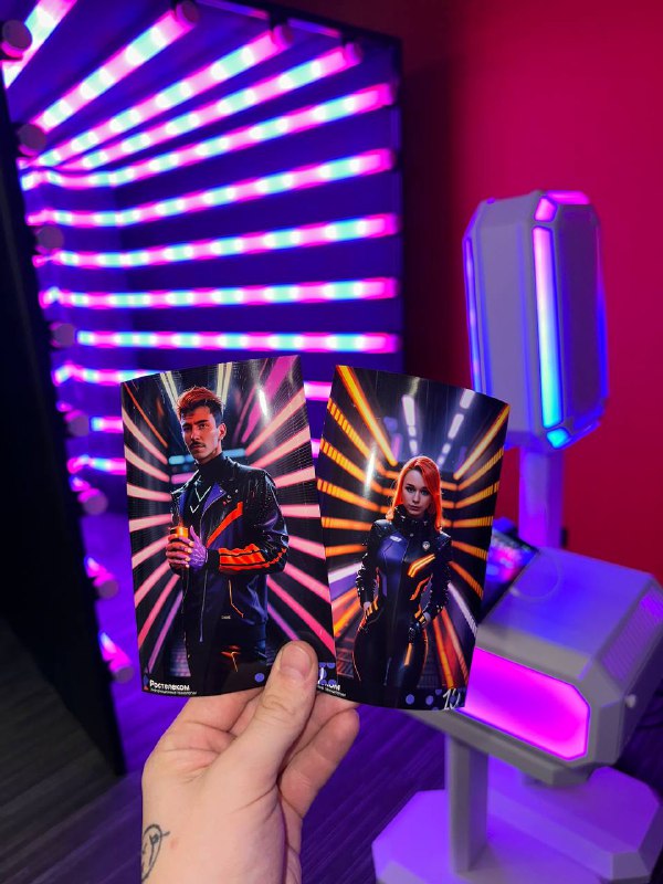 Рука держит две печатные фотографии на фоне неонового туннеля и светящейся фото-стойки MixАп — яркие пурпурно‑синие огни.