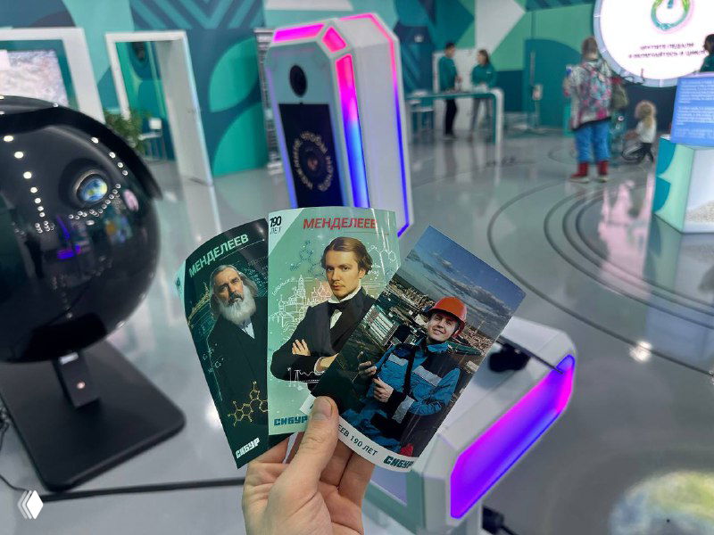 Рука держит распечатанные фотографии из интерактивной AI‑фотозоны на фоне выставочного стенда с подсветкой и киоском, демонстрация сервиса.