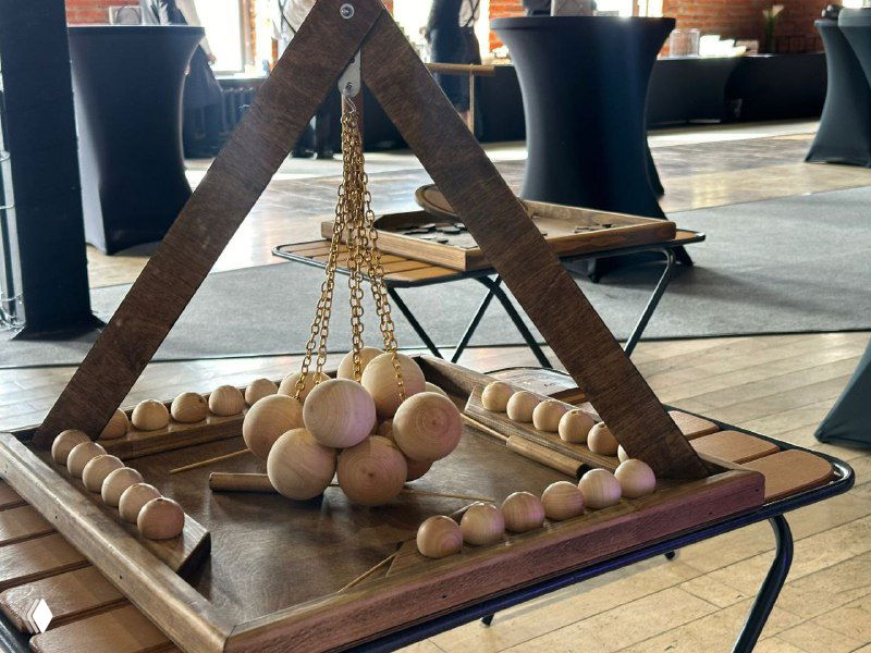Набор деревянных настольных игр, установленный на столе в локации мероприятия: треугольная рамка, деревянные шарики и бусины в кадре.