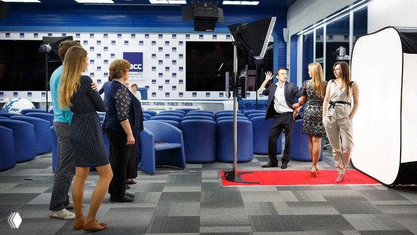 Флипбук‑фотозона в помещении: гости на красной дорожке перед белым портативным фотофон‑кубом, видно световое оборудование и оператора.