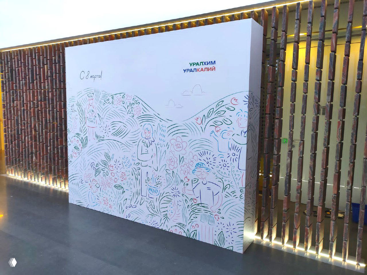 Белый пресс‑волл с авторским цветочным рисунком и логотипом «Уралхим / Уралкалий», установлен в современном интерьере рядом с декоративной стеной и подсветкой