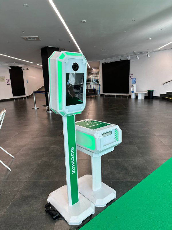 Белая и зелёная фотостойка MixAp в зале: стойка с экраном, встроенным принтером и цветной подсветкой, установленная для мероприятия.