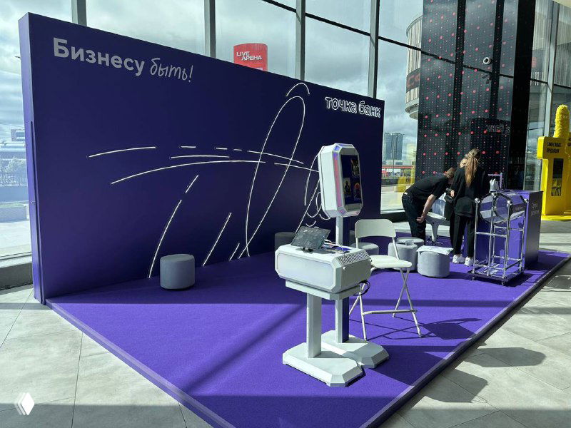 Выставочная зона с фиолетовым брендингом и установленной супер‑мощной фотостойкой: стойка, стол и вид экспозиции в зале.