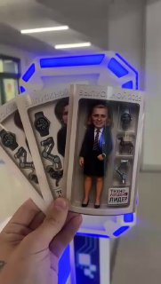 Рука держит несколько упаковок с коллекционными мини‑фигурками на фоне подсвеченной фотостойки Toy‑Box — демонстрация результата ИИ‑обработки для мероприятия.