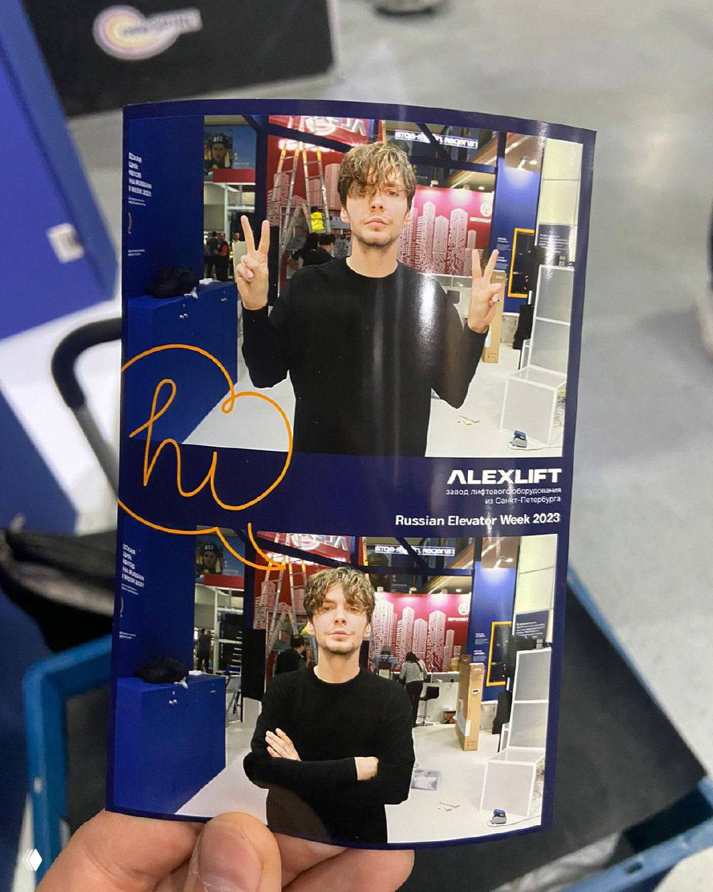 Распечатанная фотополоска в руках: две фотографии молодого человека с жестом «V», логотип ALEXLIFT и оформление выставочного стенда на заднем плане.