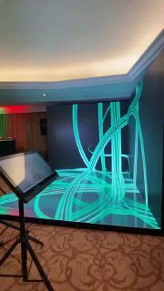 Фотозона Bullet Time: неоновая 3D‑анимация, проецируемая на стену и пол в зале мероприятия, перед ней стоит стойка с тачскрин‑панелью управления.