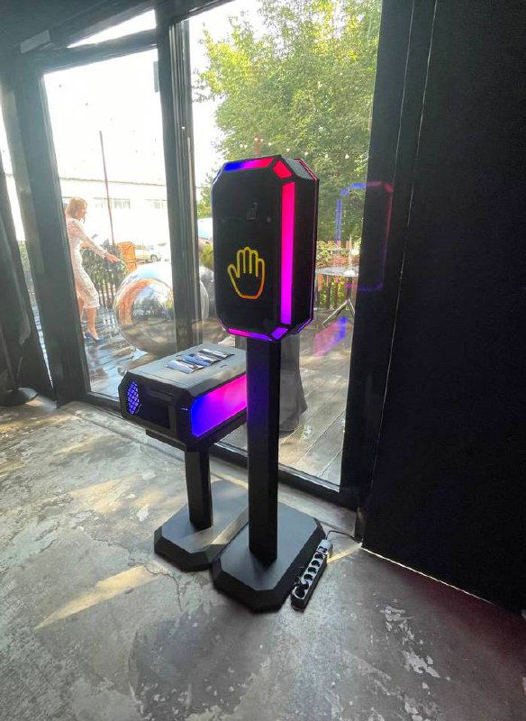 Сенсорная стойка Tech-Scan в интерьере: высокий черный корпус с подсветкой и иконкой ладони на панели, установка для ивента рядом с окном.