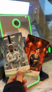 Рука держит две напечатанные фотокарточки на фоне селфи‑зеркала Hi‑Tech с яркой зелёной подсветкой; видна часть стойки и отпечатанные портреты гостей, демонстрация печати.