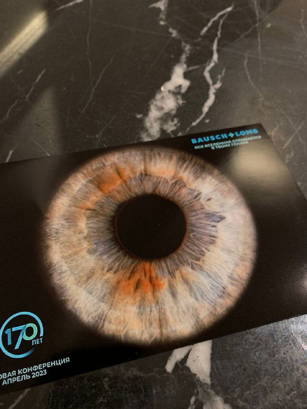 Макро‑фото радужки глаза на печатной карточке — крупный план радужки с коричневыми и голубыми оттенками на тёмном фоне, пример услуги для мероприятий