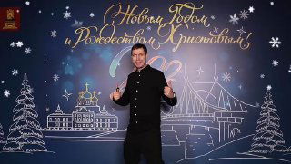 Мужчина улыбается и позирует на праздничном фоне с иллюстрацией города и надписью «С Новым годом и Рождеством Христовым», атмосфера ивента и фотозоны.