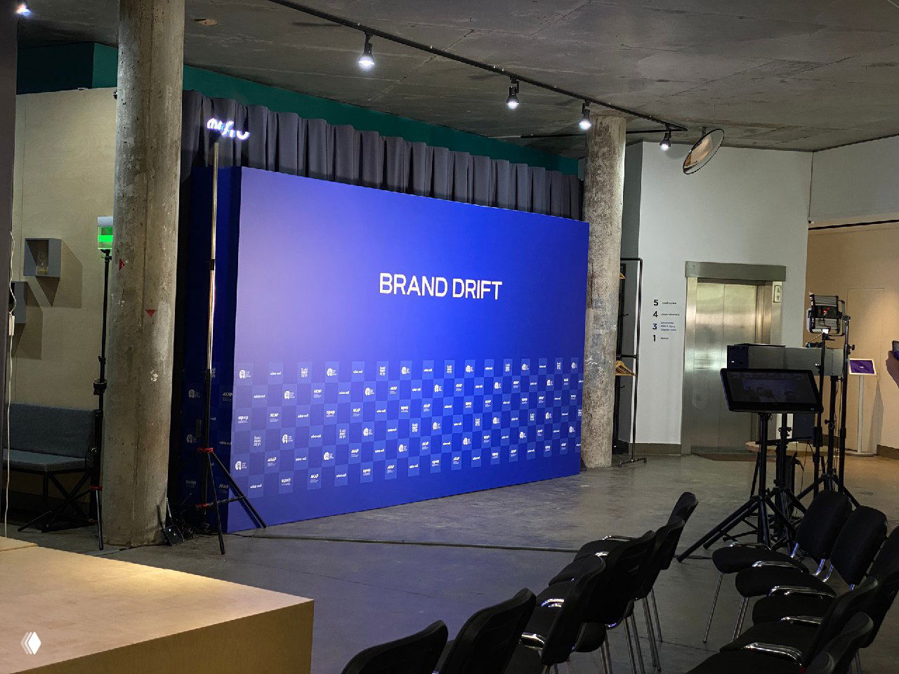 Широкий план пресс‑волла 5x3 м с надписью BRAND DRIFT в зале; рядом установлены стойки и ноутбуки для организации съемки.