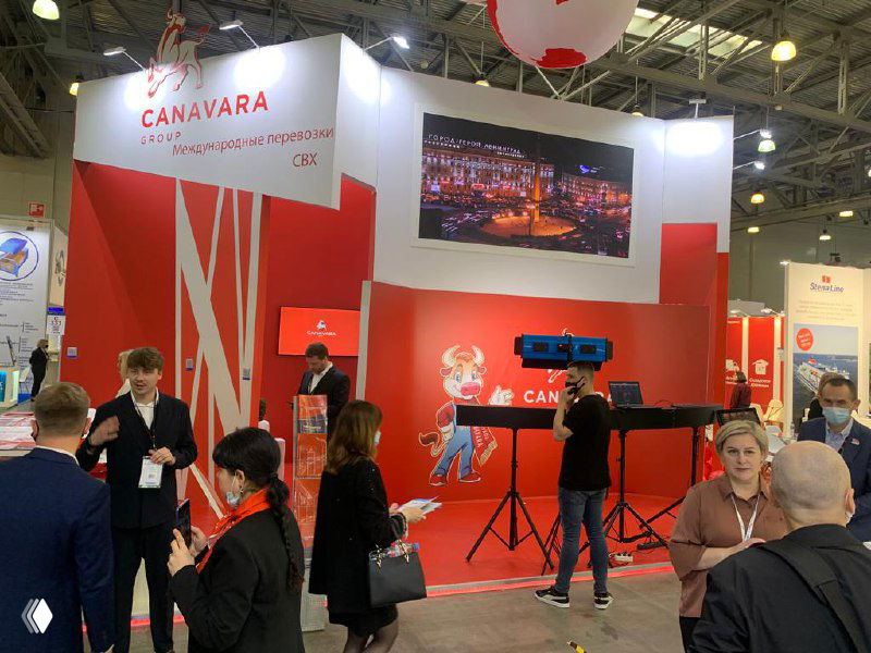 Выставочный стенд красно‑белой цветовой схемы с логотипом CANAVARA, посетители вокруг стенда и оборудование для фото и видео демонстрации услуг.