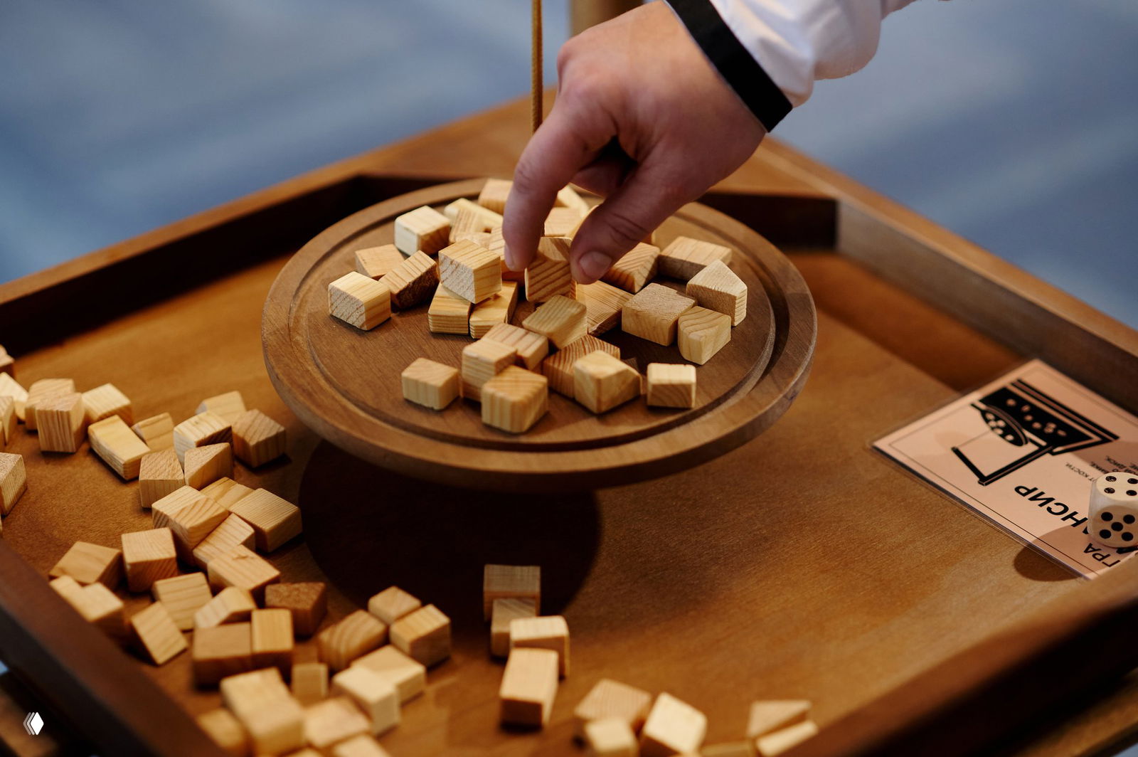 Крупный план крафтовой деревянной игры: множество маленьких деревянных кубиков на вращающейся тарелке и рука игрока, сцена мероприятия.
