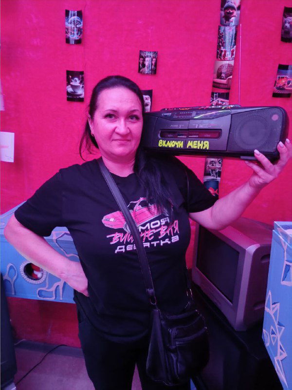 Портретная фотография мамы в развлекательной зоне квеста: она держит колонку и улыбается, семейный момент во время выхода на экскурсию и квест.