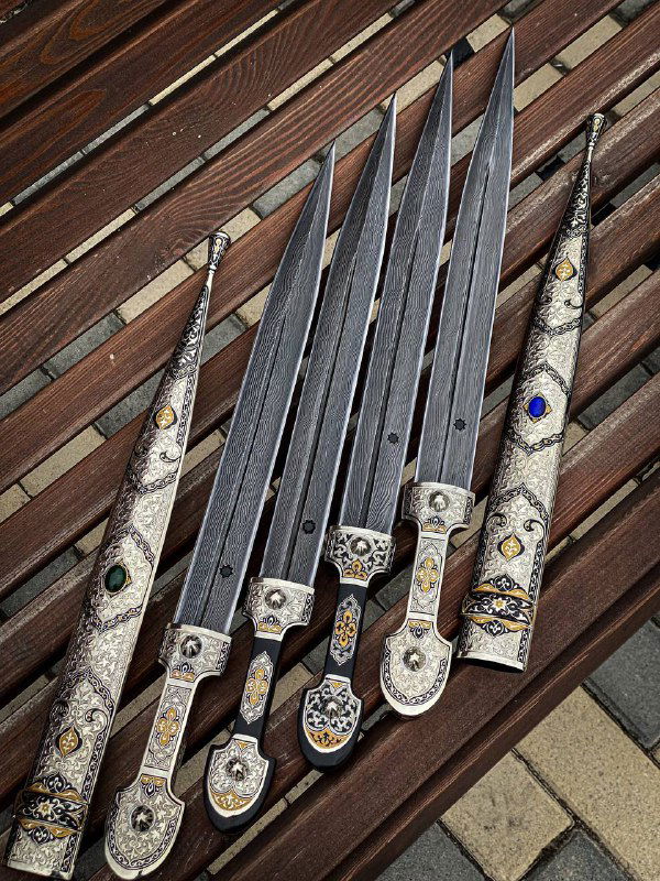 Кинжалы в ножнах на деревянном фоне, акцент на рельефные узоры дамаска по всей длине клинков и на декоративные элементы мельхиоровых ножен.