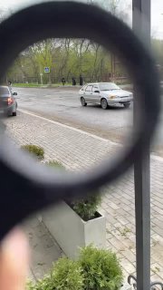 Кадр через кольцо керамбита: в фокусе кольцо и часть рукояти, в фоне проезжая часть с автомобилем и городской тротуар.