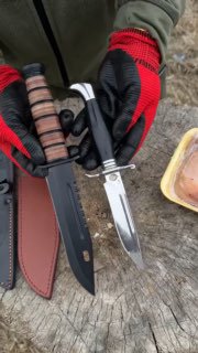 Человек в перчатках держит два ножа: тёмный тактический с деревянной насадкой на рукояти и блестящий клинок с мельхиоровой гардой на походном фоне.