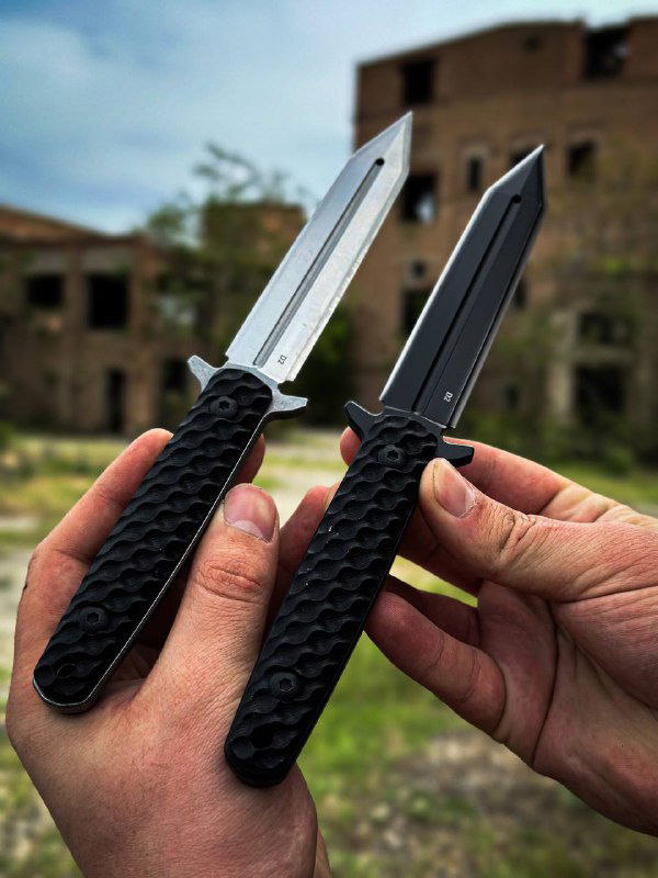 Крупный план двух тактических клинков: один серебристый, другой в черном покрытии; рукояти с накладками J10 и отчетливой текстурой.