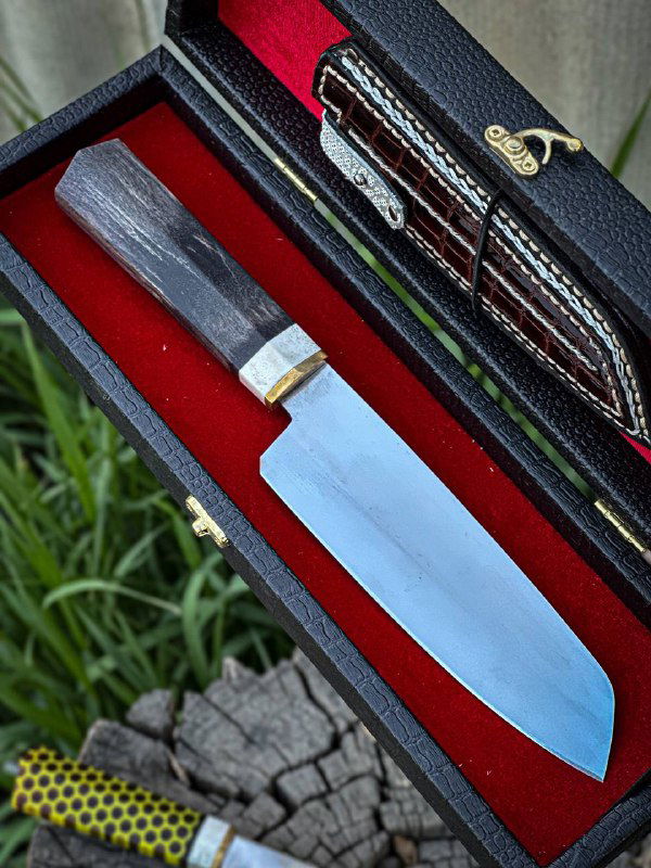 Крупный план кухонного ножа в футляре: гладкое лезвие и тёмная рукоять, аккуратная отделка и контраст красного бархата футляра.