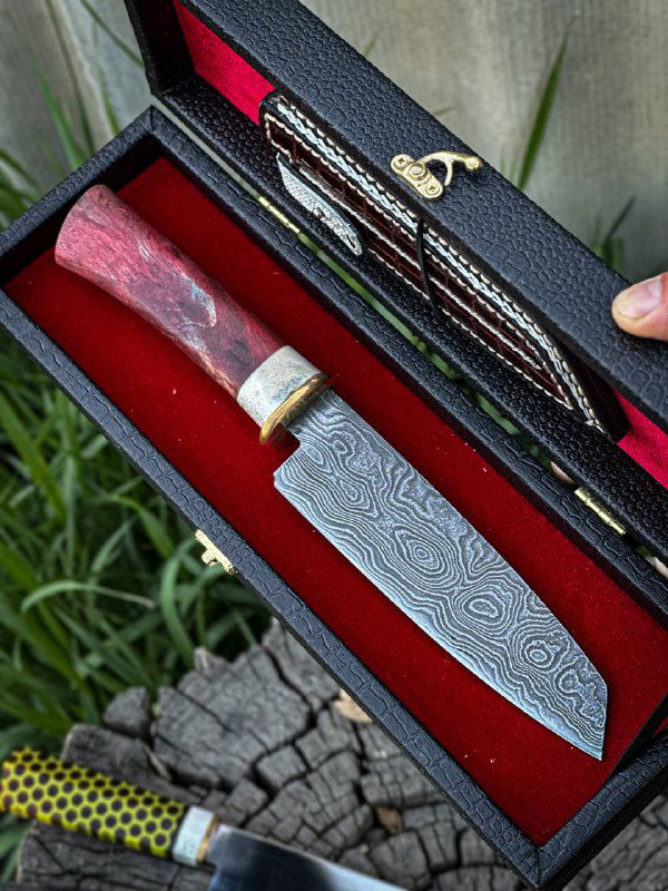 Кухонный нож с дамасковым узором клинка и красной рукоятью в футляре; вид, подчёркивающий структуру дамасской стали.