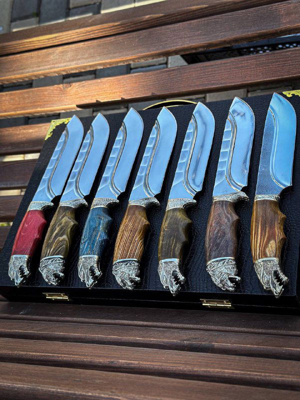 Групповой снимок ножей под углом: заметны одинаковая форма клинков, декоративные гарды и разнообразие оттенков стабилизированной карельской берёзы на рукоятях