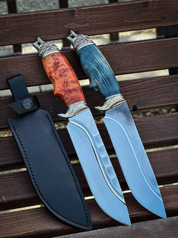 Два ножа рядом с кожаными ножнами: один с яркой красной рукоятью, другой с тёплой древесной текстурой; показаны вариации отделки и посадки клинка в рукоять