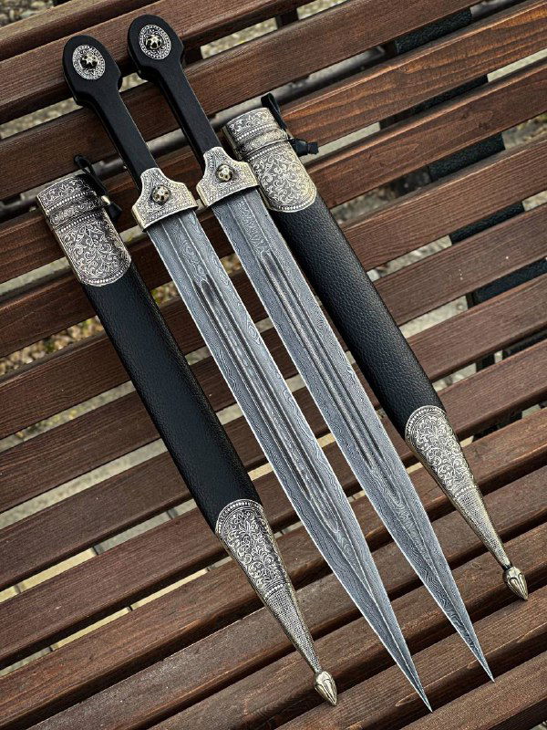 Три кинжала в ножнах на деревянной скамье под углом; хорошо видны наконечники ножен и декоративная гравировка мельхиоровых деталей