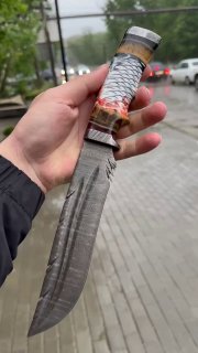 Крупный план рукояти ножа «Перо» с заметной вставкой бивня мамонта, декоративной шишкой в акриле и деталями литья дамаска на фоне улицы.