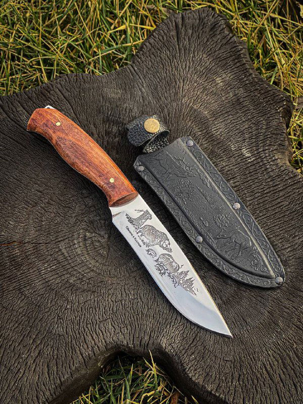 Охотничий нож «Охотник» с рукоятью из кавказского ореха лежит рядом с черными ножнами на шкуры, снимок сверху на траве.