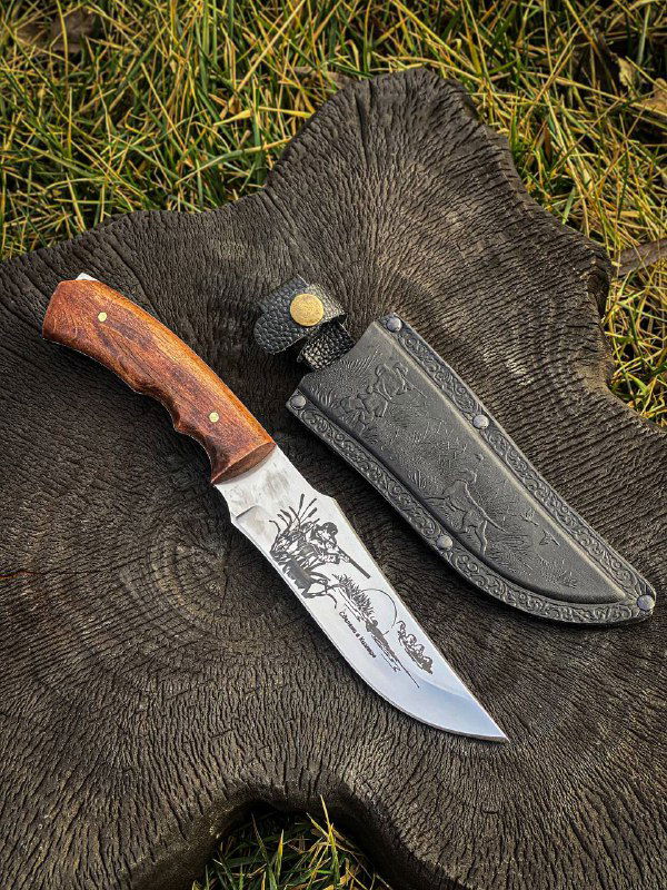 Нож с гравировкой на лезвии и деревянной рукоятью на фоне шкуры, акцент на форму клинка и отделку привалочной части.