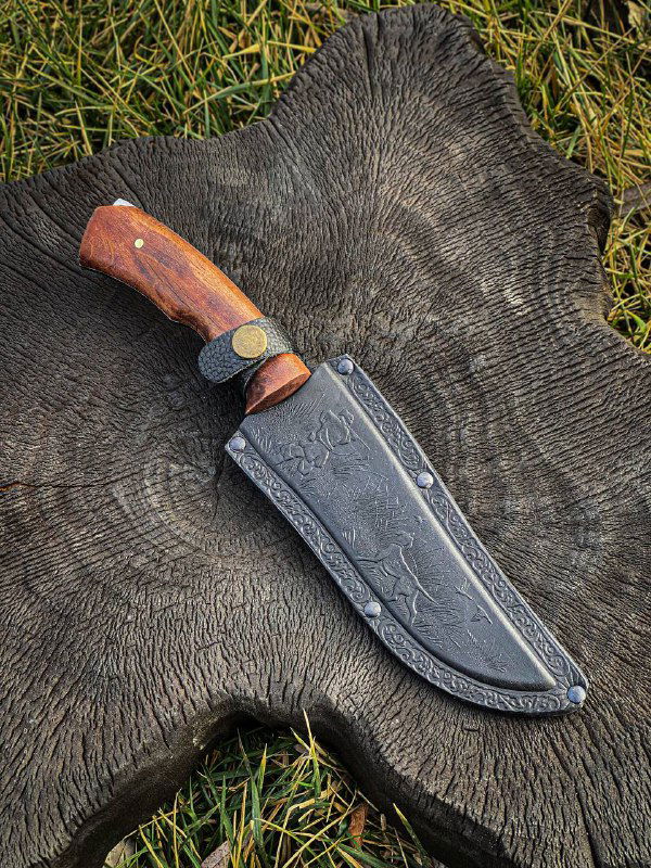 Нож в ножнах на фоне шкуры и травы, снимок сверху демонстрирует общие пропорции и отделку ножен и рукояти.