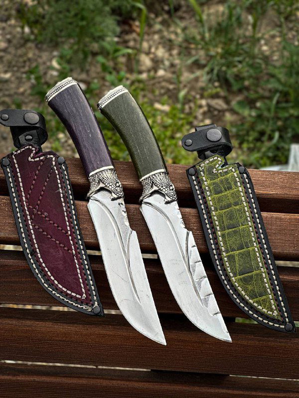 Три ножа в ножнах с акцентом на текстуру стабилизированной карельской берёзы разных цветов и декоративную отделку кожаных ножен.