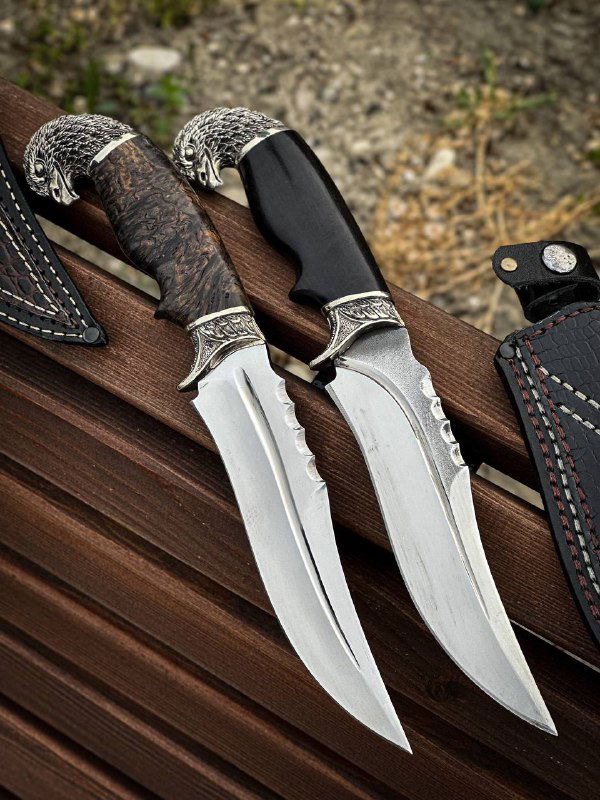 Крупный план двух клинков и рукоятей: видно форму гарды, заточку и контраст чёрной рукояти с деревянной на фоне скамьи.