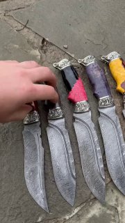 Рука прикасается к серии ножей «Скорпион»: крупный план показывает структуру дамасской стали, мельхиоровые украшения и текстуру разноцветных рукоятей на каменном фоне.