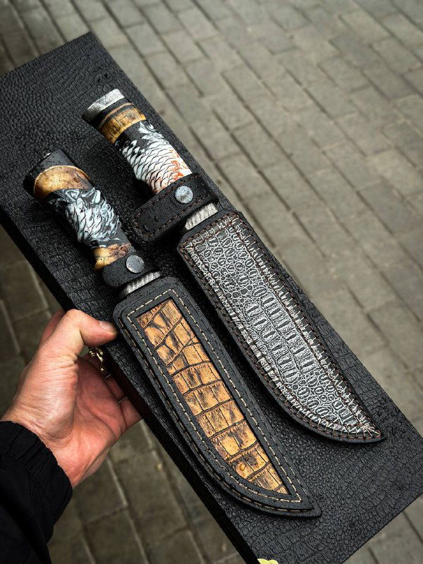 Два ножа в чёрных кожаных ножнах: текстура кожаных ножен с декоративной вставкой и вид рукоятей с бивнем мамонта, на фоне рабочего подноса.