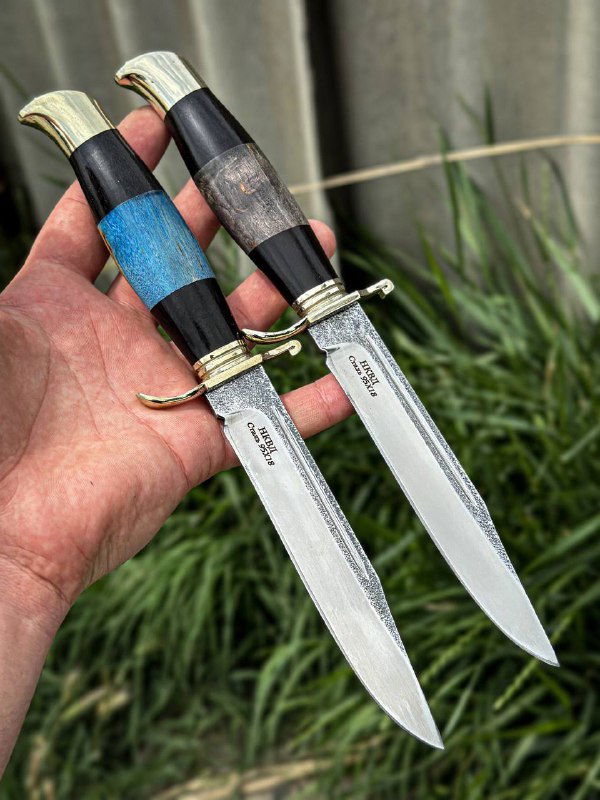 Две финки НКВД в руке: рукояти синего и тёмно-серого цветов, видна текстура стабилизированной древесины и чистый обух клинка.