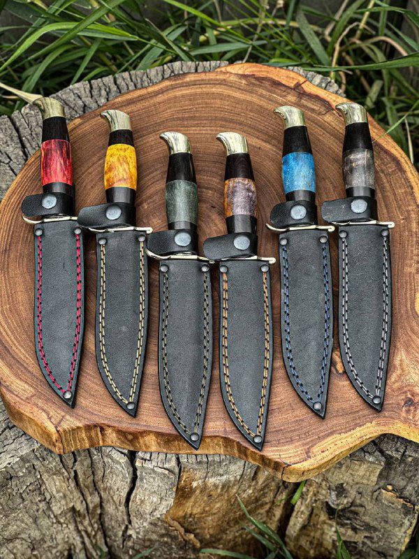 Комплект финок НКВД с кожаными ножнами: пять ножей с разноцветными рукоятями на фоне травы и деревянного спила.