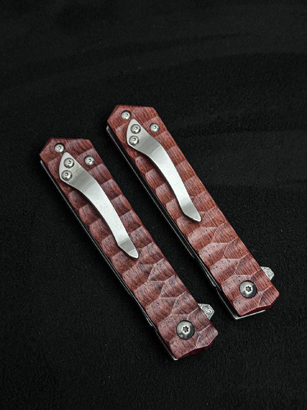 Обратная сторона двух складных ножей с металлическими клипсами и винтовыми креплениями; вид на текстурированные деревянные рукояти тёмно‑красного цвета и монтаж клипс.