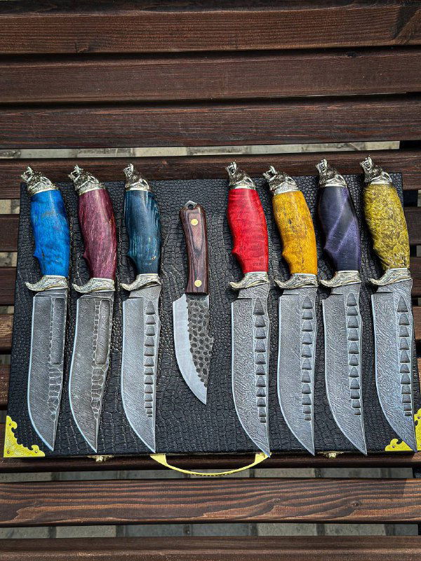 Широкий план ряда ножей «Волк»: одинаковая форма клинков, характерная насечка и разноцветные рукояти из стабилизированной карельской берёзы.