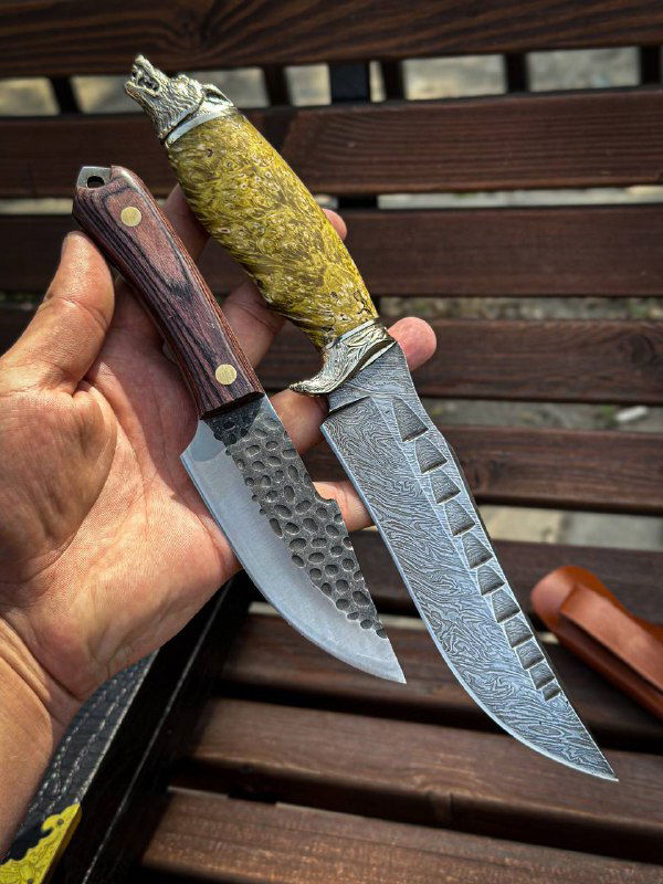 Рука держит два ножа «Волк»: один с текстурной поверхностью клинка и жёлтой рукоятью, другой с тёмной деревянной плашкой — видна деталь фурнитуры.