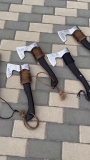 Вид сбоку на пару топоров с травленным лезвием и тёмными рукоятями; акцент на форму топора и декоративное оформление лезвия на фоне плитки.