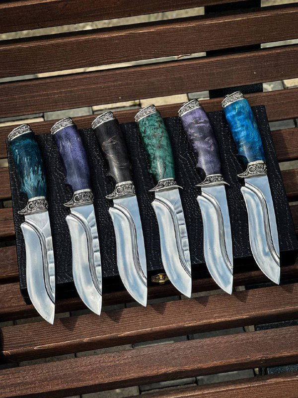 Ряд ножей на деревянной скамье: несколько клинков 95х18 с разноцветными стабилизированными карельскими рукоятями и одинаковой декоративной гардой.